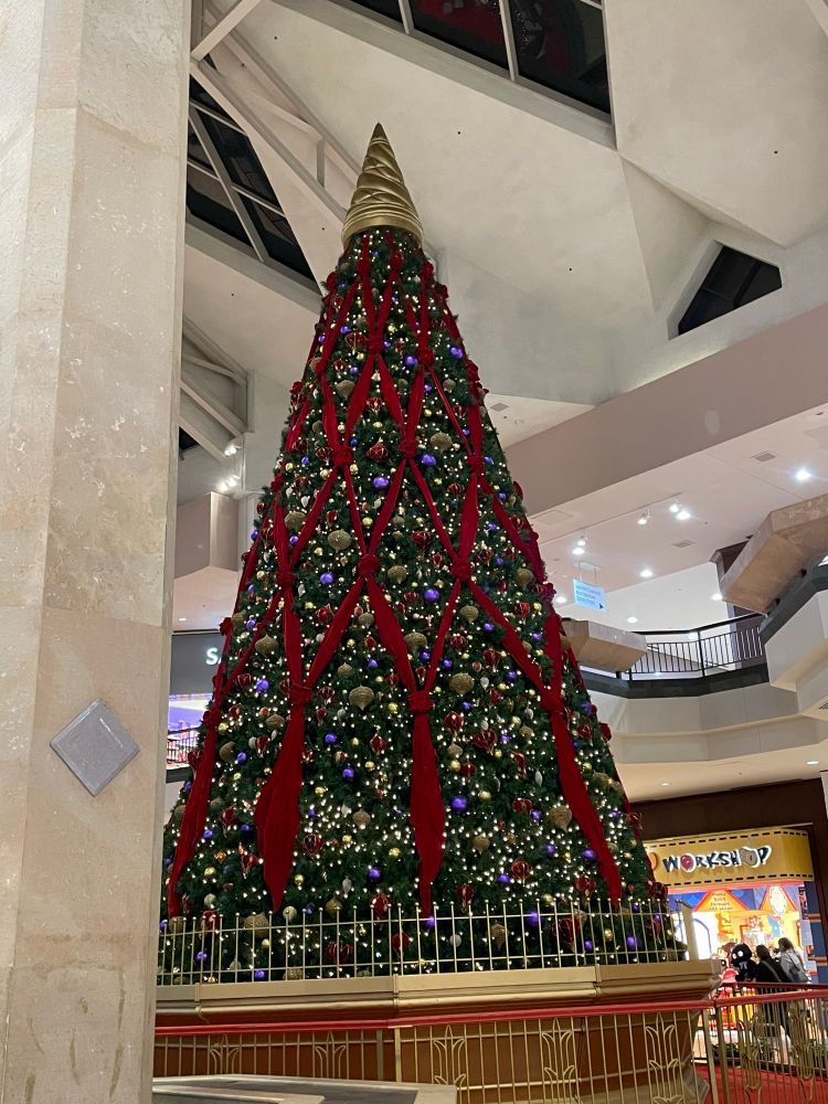 A giant Christmas tree that is fully decorated inside the center of the mall next to a Build a Bear Workshop