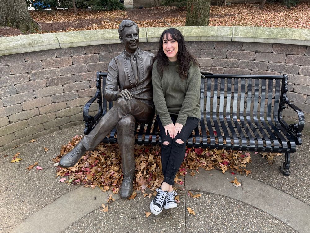 A woman sitting on a bench next to a Mister Rogers statue.