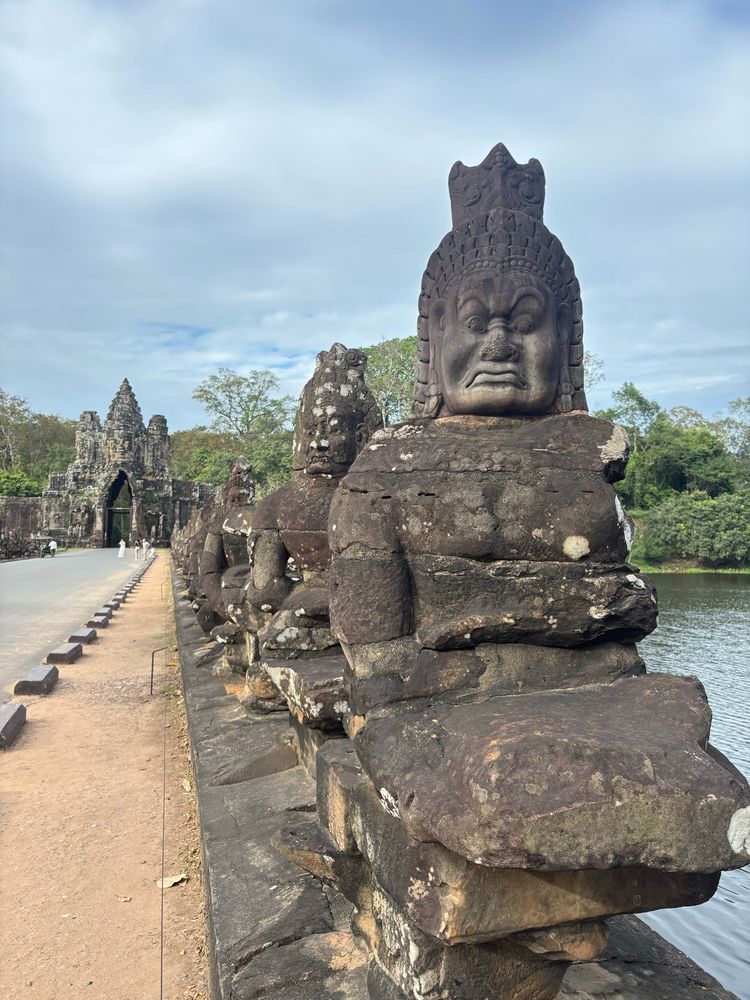 Statues lining the right hand side of the picture. From the first one, we can see that it is a creepy guy with an angry face - a demon. To the left of the picture a stone gate in the distance 