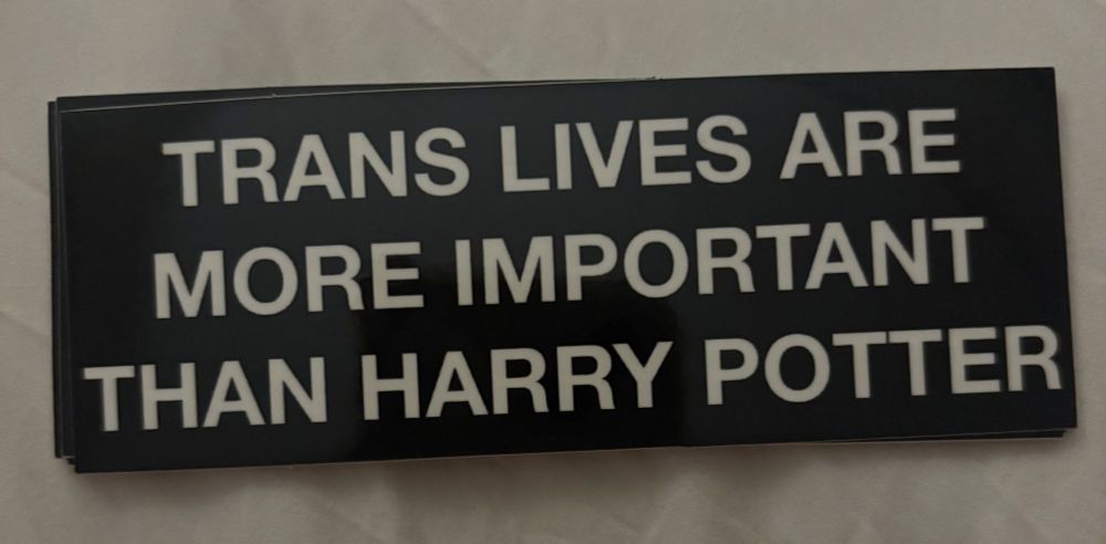 Black sticker with white writing in block capitals: TRANS LIVES ARE MORE IMPORTANT
THAN HARRY POTTER