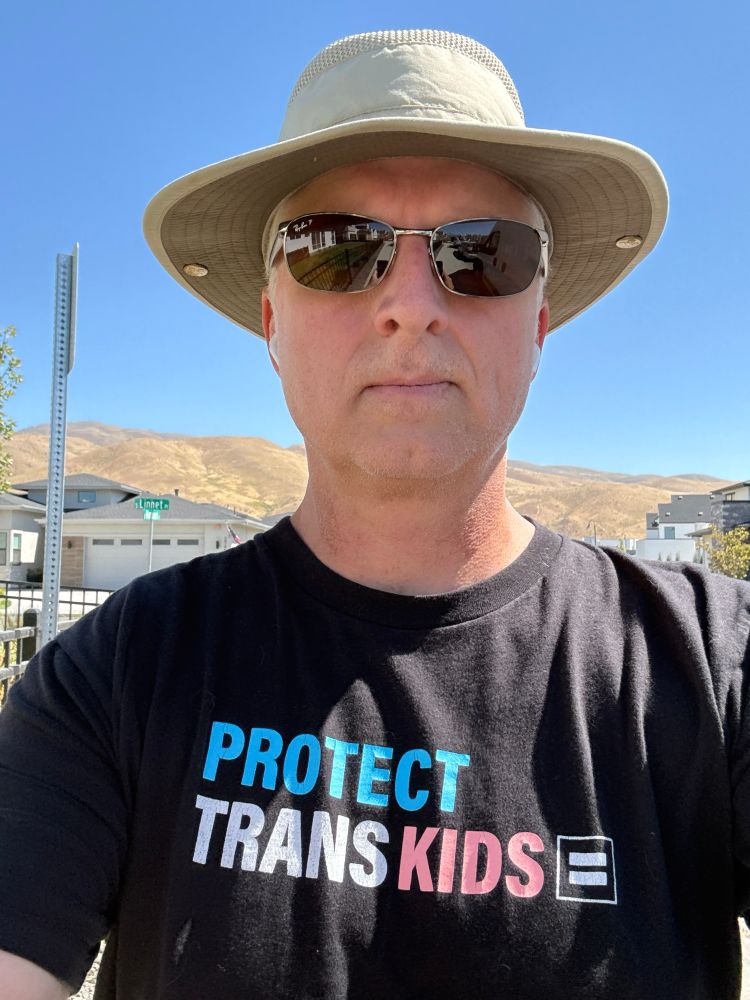 Selfie out for a walk wearing a wide brimmed hat and a Campaign for Human Rights tshirt that says PROTECT TRANS KIDS