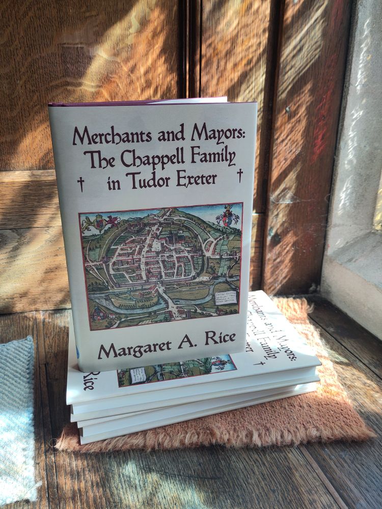 Photograph of the book, Merchants and Mayors, in the window of Tuckers Hall, Exeter. It is a hardback book with a beige dustjackets featuring a 16th century map of Exeter and the title and author in burgundy type.