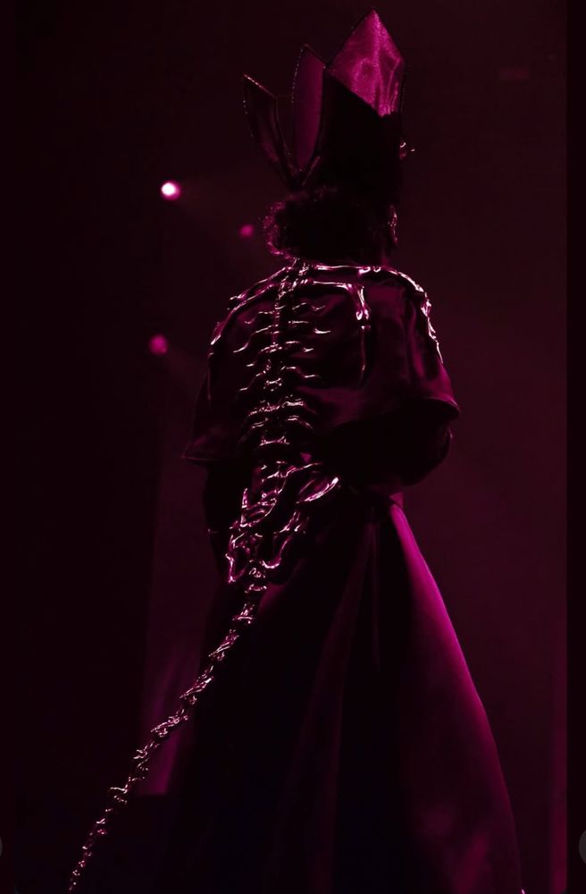 Screenshot of Papa V on stage wearing his outfit with metallic bones, the spine leads to a tail. Its very cool