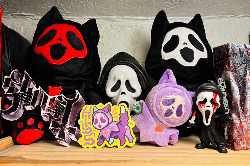 Shown is my ghost face collection, on the left is a devil ghostcat plush by steelwithteeth, in front of it is my the band Ghost glasses, in the middle is my ghost face popcorn bucket, in front of the bucket id the new addition, zombie ghostcat with a sticker. On the right is another ghostcat plush by steelwithteeth and a ghostface youtooz figure.