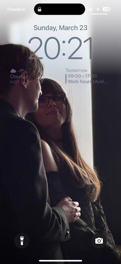 Photo of myself on the left in a black suit jacket and my wife on the right in a black lace dress during our wedding reception. I will never be normal about this photo lol