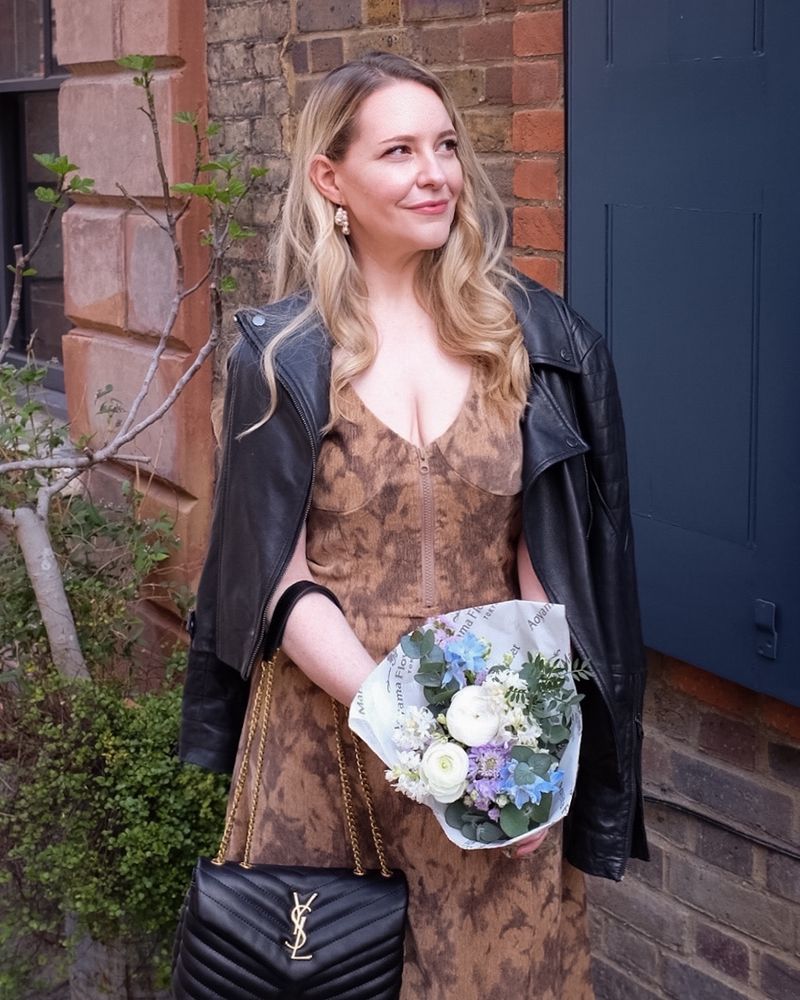 A photo of Geri taken yesterday in Spitalfields, London. She's wearing a lovely dress, with a jacket draped around her shoulders; she's holding flowers and smiling.