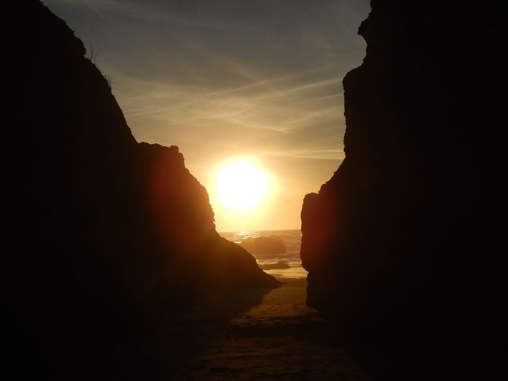 Fort Bragg, CA. The sun is setting over the ocean. I took this photo standing between two large rock outcrops on the beach. Photo by me.