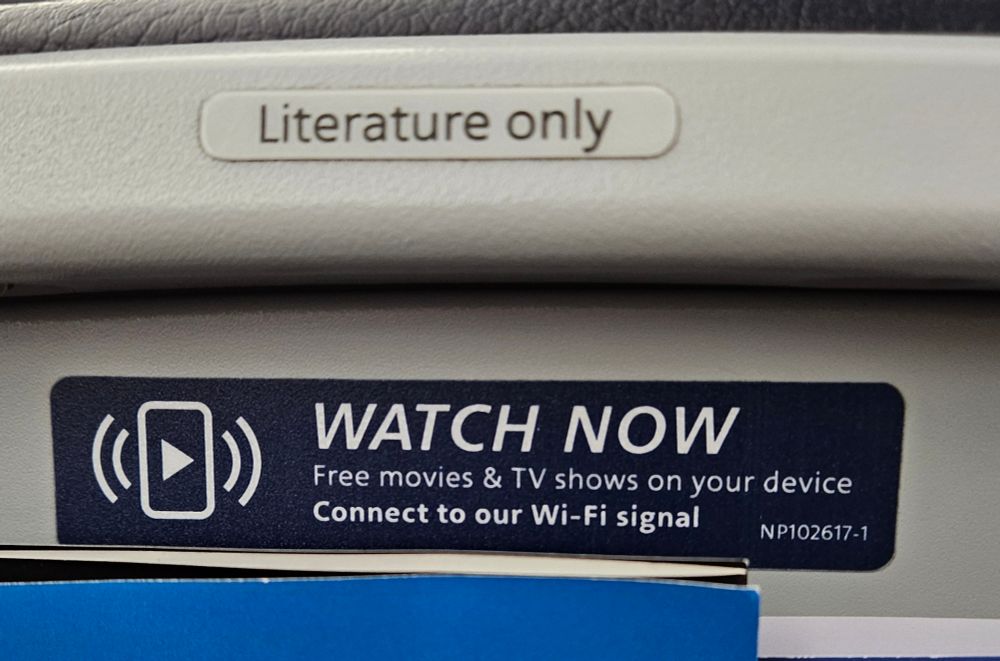 Back of airline seat with a sign reading "Literature only" and another sign reading "WATCH NOW, Free movies and TV shows on your device."