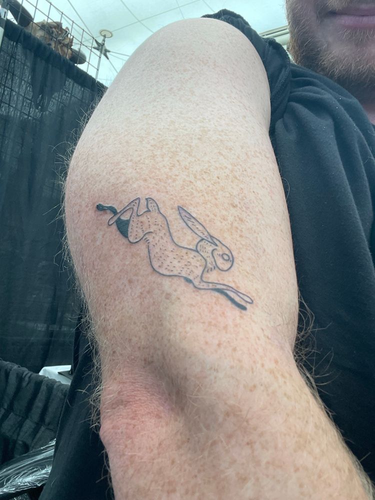 A black-ink tattoo of a wild-eyed hare