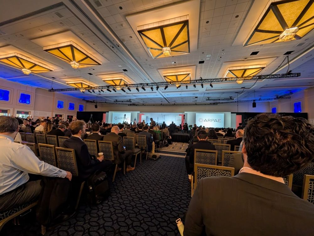 A conference hall at a convention center taken from near the back of the room, looking towards the stage 