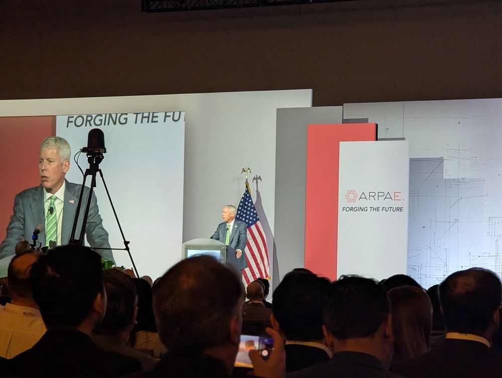 A man (DOE secretary Chris Wright) giving remarka at a podium in front of an American flag pole and a banner for the conference ("ARPA-E: forging the future")