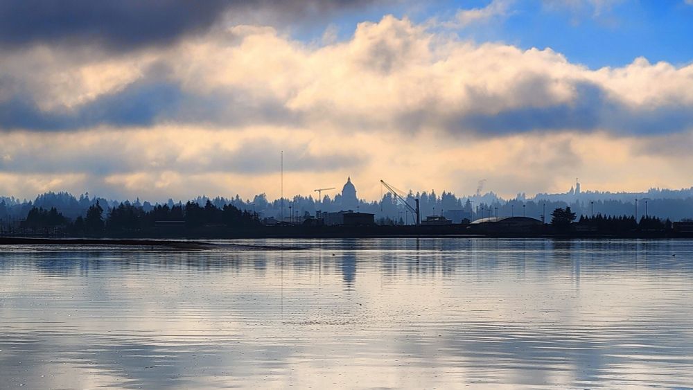A view of the Washington State Capitol building from Squaxin Park in Olympia, WA. The Capitol and sky are reflected in bay.