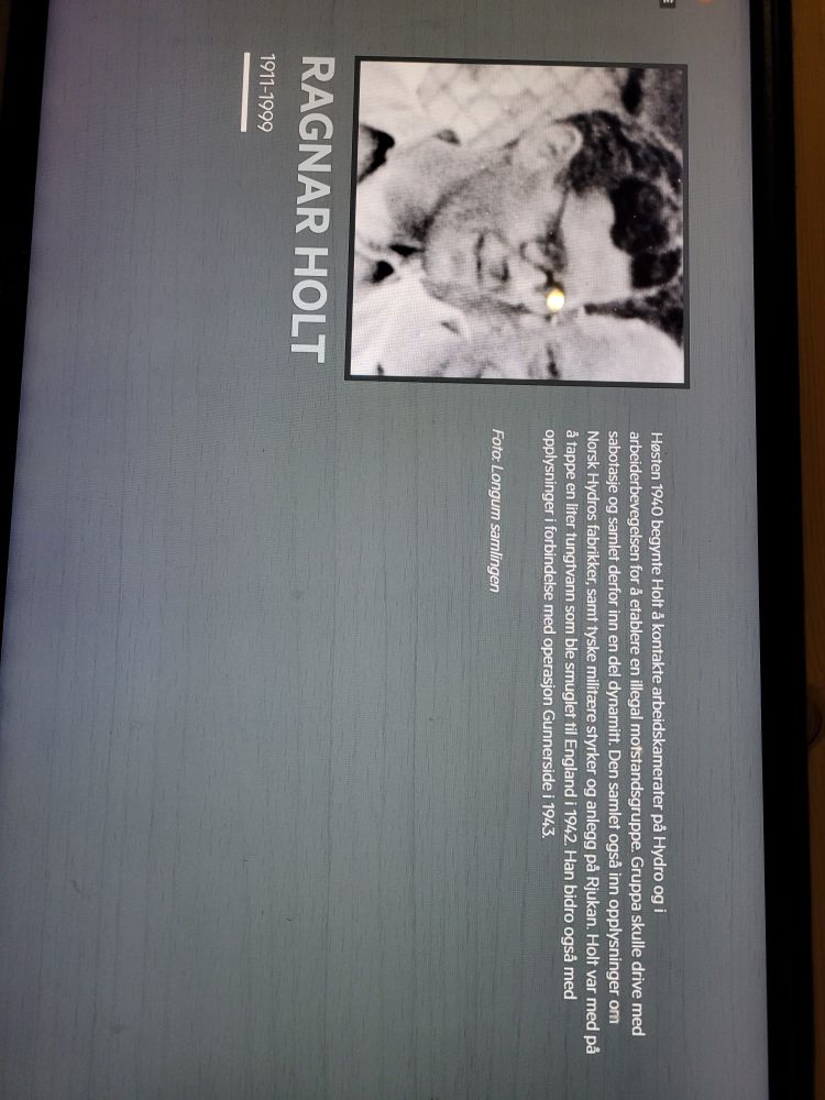 A photo of Ragnar Holt, a Norwegian who was part of the Norwegian resistance during Nazi occupation during WW2. There is accompanying text in Norwegian which describes his role. This photo hangs in the factory where he worked (now a museum) in Vemork, near Rjukan Norway. 