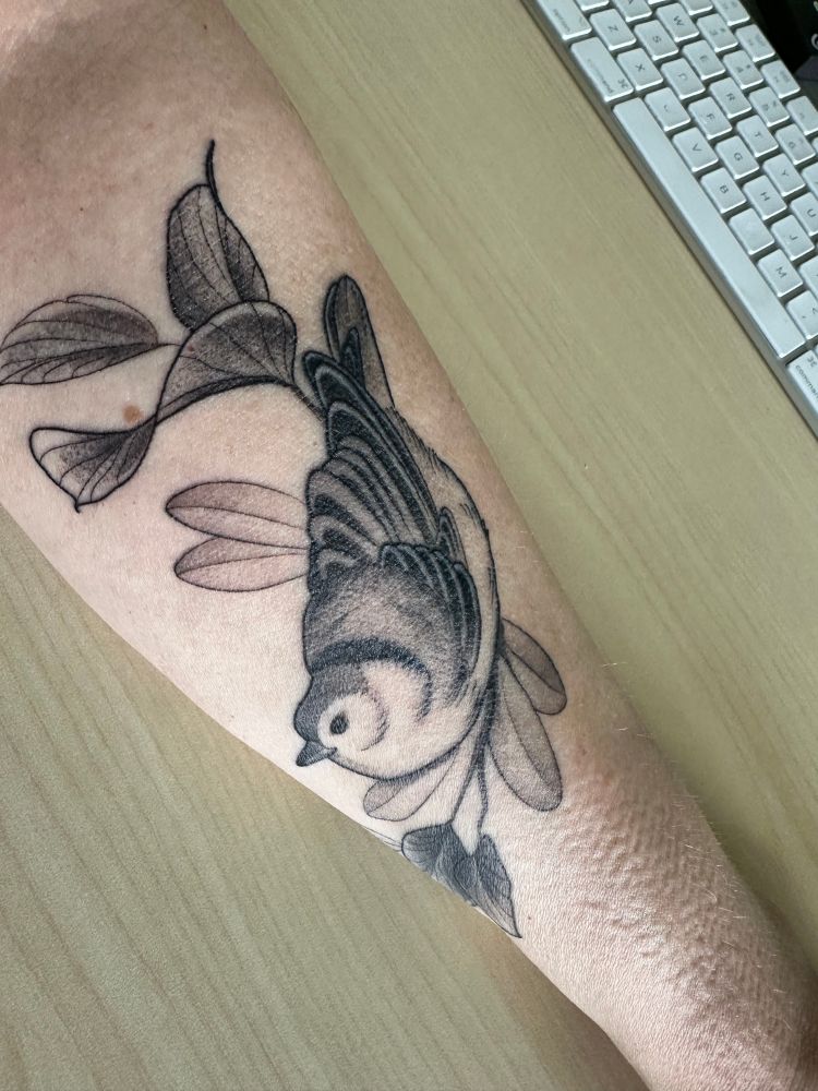 Forearm of a white person with a tattoo of a white-breasted nuthatch. This angle shows that the body is perched in the characteristic upside-down pose of a nuthatch.