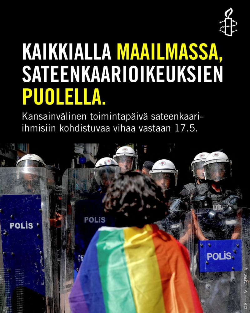 Joukko mellakkapoliiseja, joiden edessä sateenkaarilippuun kietoutunut ihminen. Teksti "Kaikkialla maailmassa, sateenkaarioikeuksien puolella. Kansainvälinen toimintapäivä sateenkaari-ihmisiin kohdistuvaa vihaa vastaan 17.5." 