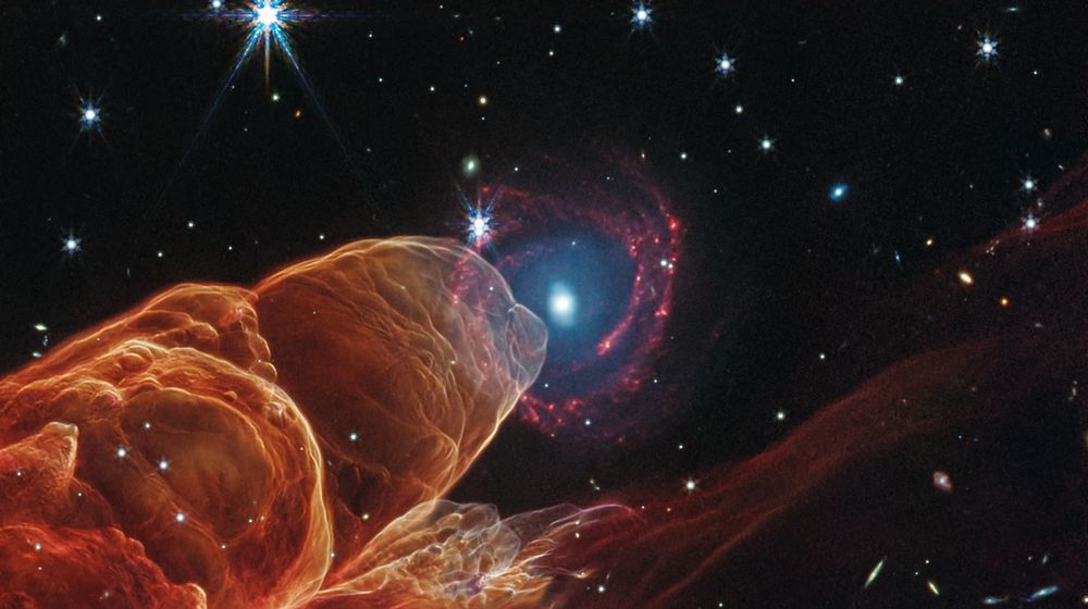 "NASA’s James Webb Space Telescope observed Herbig-Haro 49/50, an outflow from a nearby still-forming star, in high-resolution near- and mid-infrared light. The young star is off to the lower left corner of the Webb image.  Intricate features of the outflow, represented in reddish-orange color, provide detailed clues about how young stars form and how their jet activity affects the environment around them. A chance alignment in this direction of the sky provides a beautiful juxtaposition of this nearby Herbig-Haro object (located within our Milky Way) with a face-on spiral galaxy in the distant background."