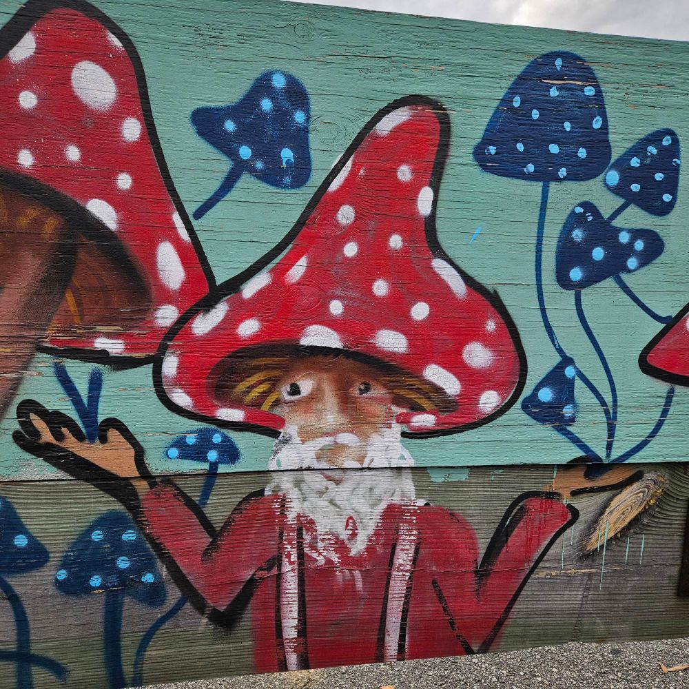 a painted mural gnome in a mushroom hat looks confused with their hands up