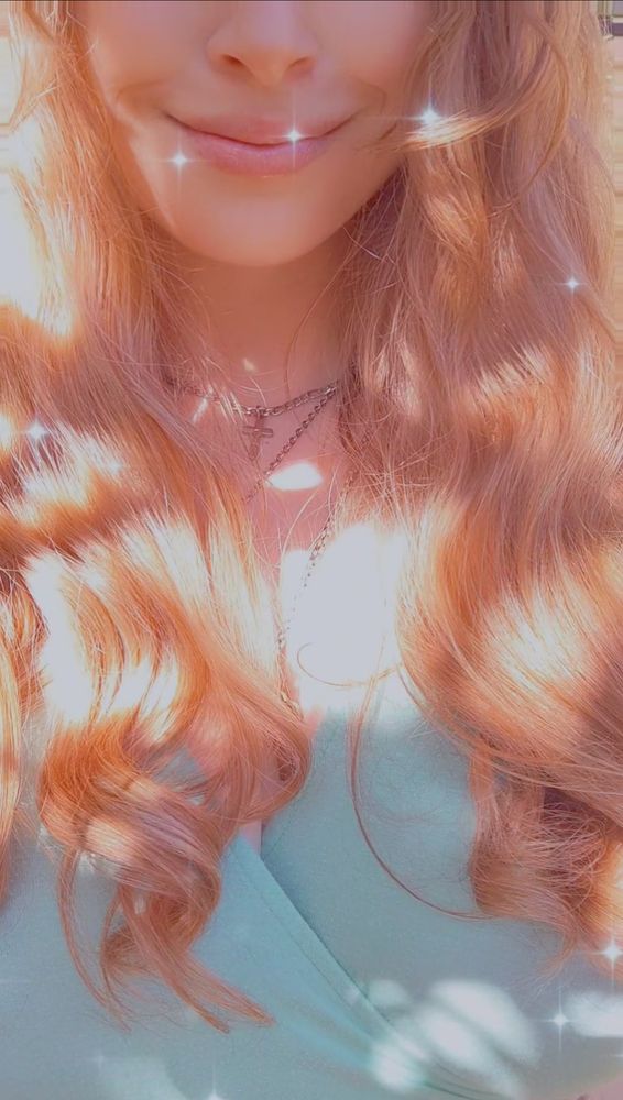 A picture showing the middle of my face to my chest. I have a filter on it that makes the sunlight look extra glowy on my hair and sprinkles sparkles around me.