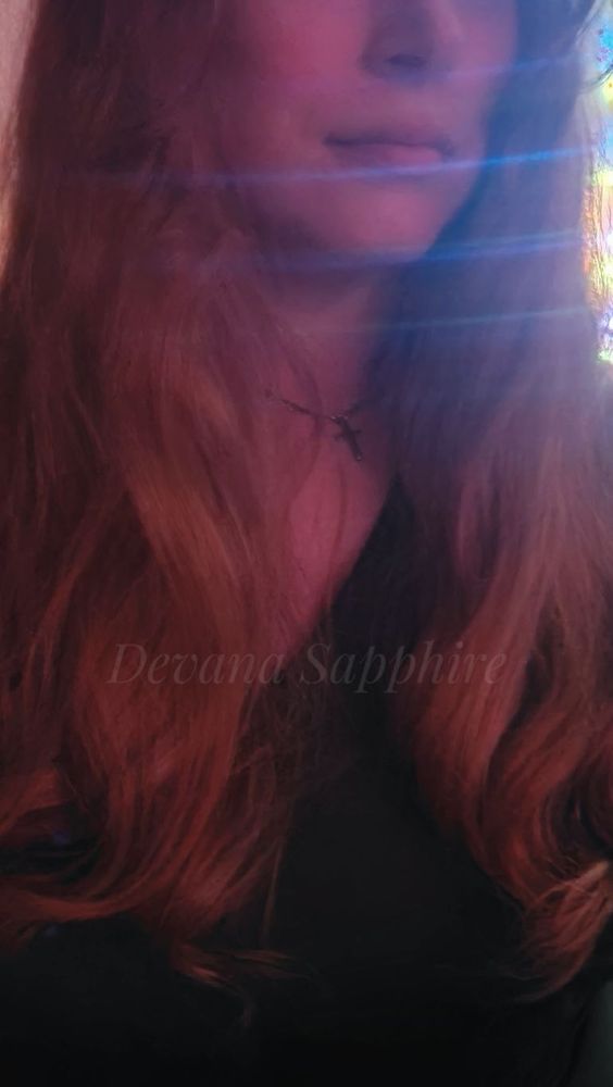 Same angle with red light. Selfie showing my long red hair falling in soft curls down my shoulders. I'm wearing a silver cross necklace and a green dress.