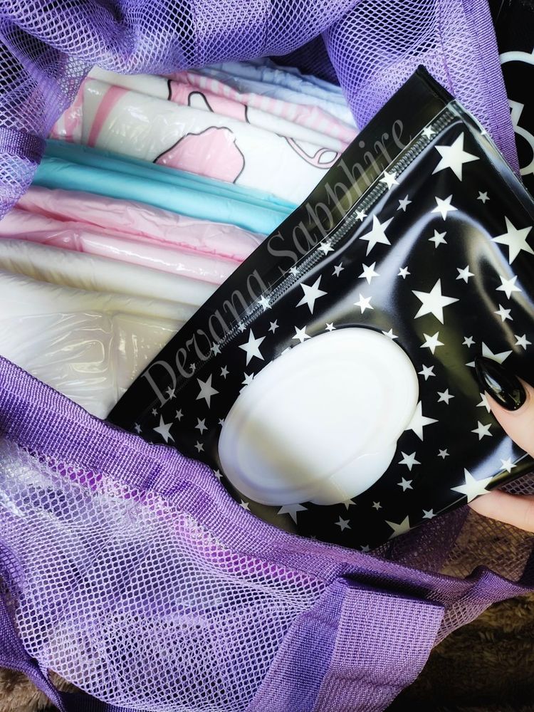My hand pulling a cute baby wipe holder, black with white stars, out of my purple mesh bag full of diapers