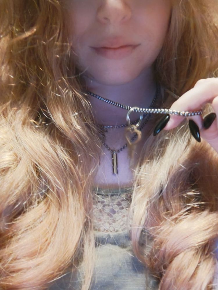 My hair framing my three necklaces with me holding up a pendant attached to one of the chains. The pendant is a heart shaped key. 