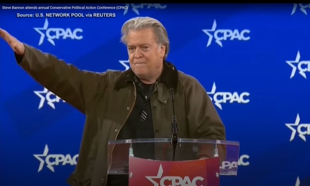 Steve Bannon throws Nazi Seig Heil Salute at CPAC at podium in front of CPAC background. 