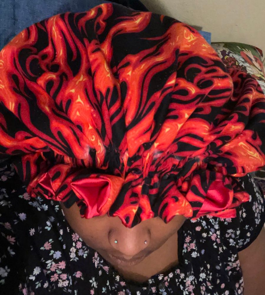 K with vertical shot and red fire/flame print bonnet with red satin lining. She is in a muumuu and the bonnet is prominent. 