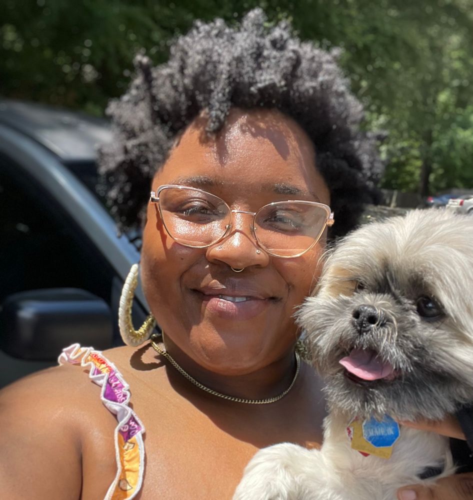 K and Mahlik standing near her car. He is a Shih tzu. She is in a bandana print dress with ruffle straps. 