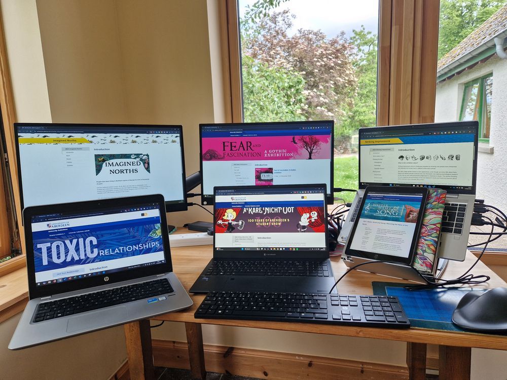 Photo of a desktop full of screens, monitors, laptops, tablets all showing different online exhibitions