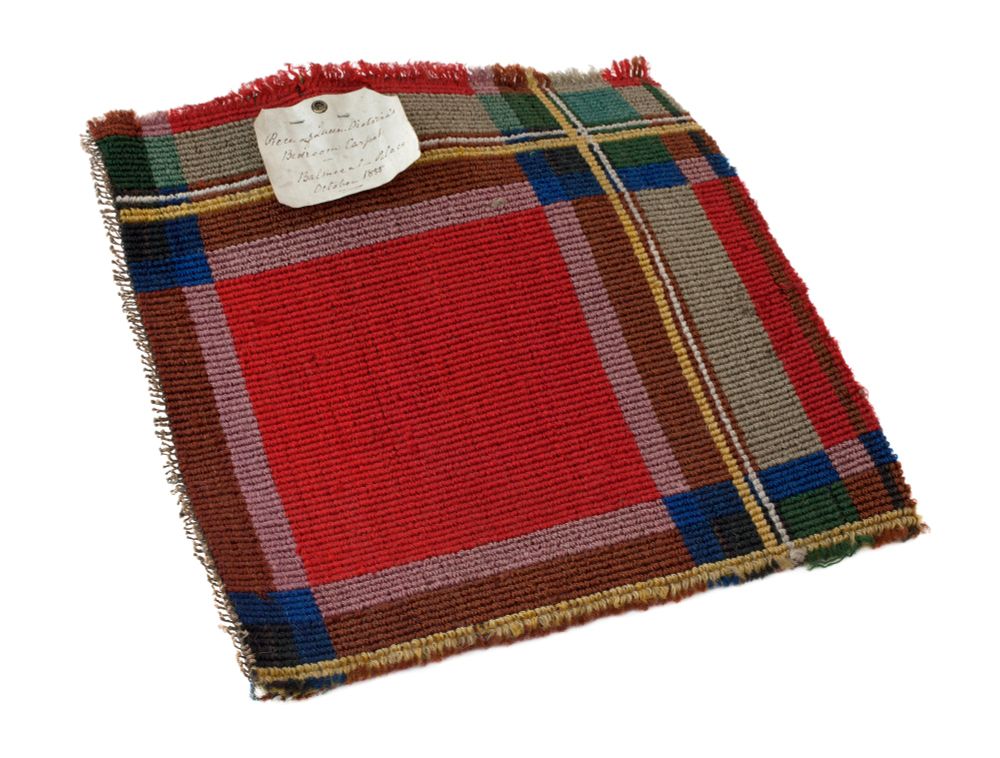 A square of red tartan carpet. There is also some Green, blue and yellow in it.