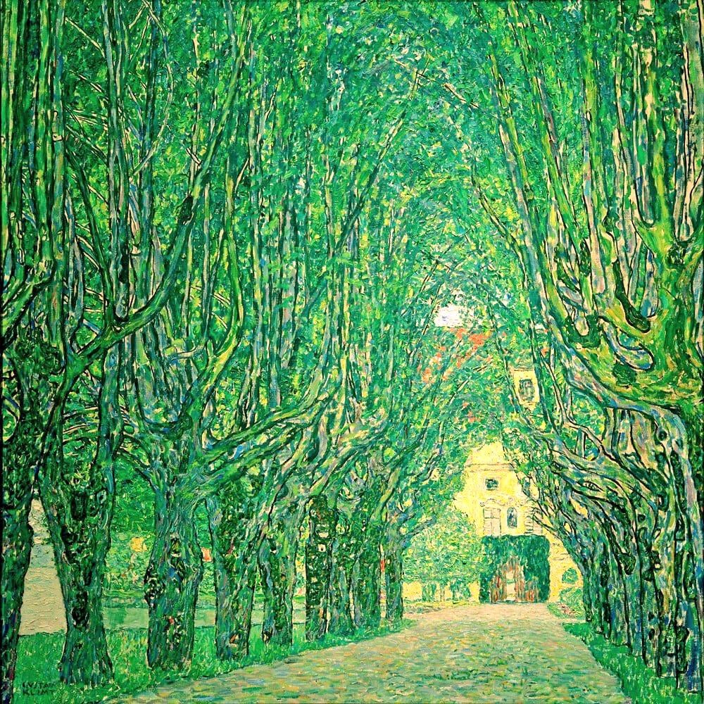 Tree-lined avenue leading to a yellow villa, with tall, dense trees forming a green canopy over the path. Sunlight filters through the leaves, creating dappled light on the ground. At the end of the avenue, a bright yellow building with arched windows and a dark entrance is partially visible. 