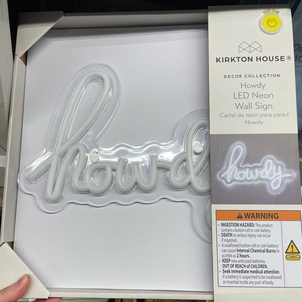 A wall sign in a white cardboard package that says “howdy” on it in a cursive font. The sign itself is clear with white LED neon lights illuminating the word.