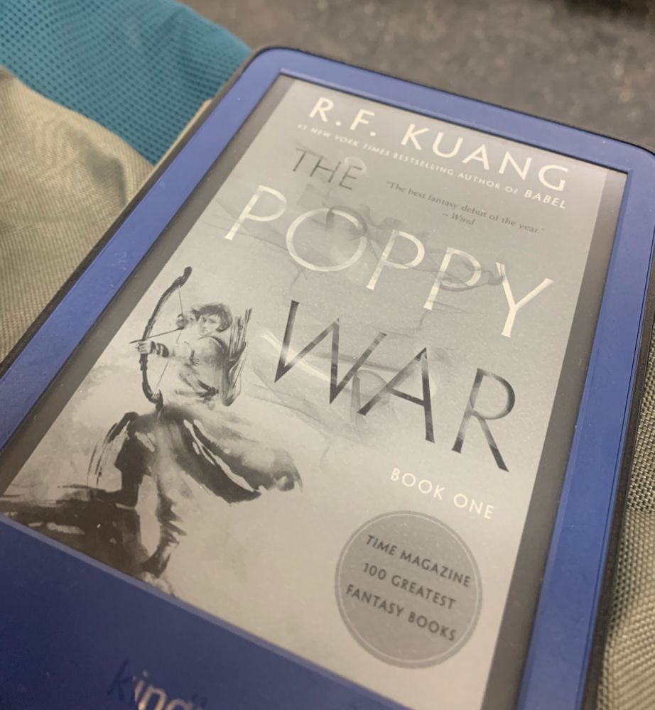 Blue kindle device, displaying the cover of “the poppy war” by R.F. Kuang. It’s a grey scale image featuring a female warrior with a bow and arrow
