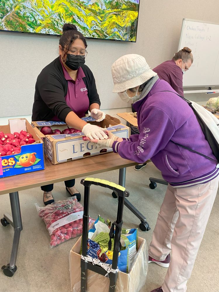 A volunteer hands a red onion to an older adult as part of Curry's grocery program. 