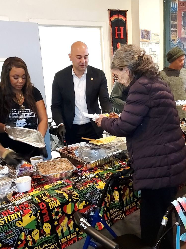 Supervisor Mahmood dishes food to a senior resident of the Cadillac Hotel.