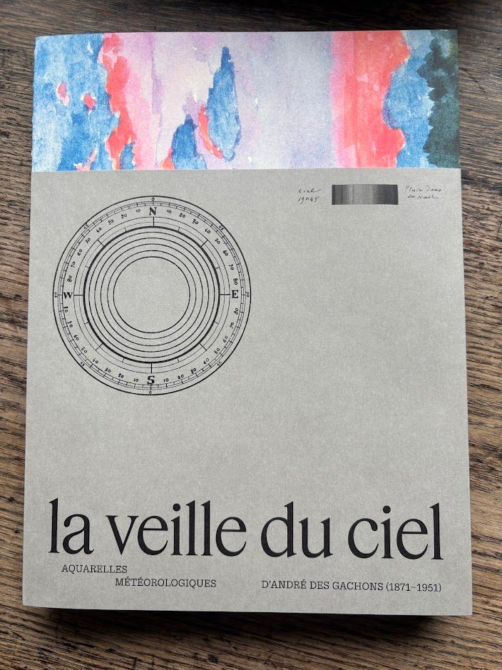 The book cover, featuring a watercolour painting of the sky in blue and red tones, with a light grey dust jacket. On the dusk jacket, there is a wind rose, as well as the title "la veille du ciel", subtitled "aquarelles météorologiques d'André des Gachons".