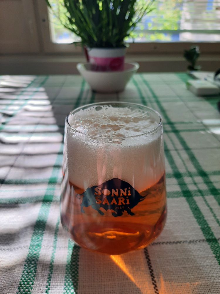 Keltaista olutta Sonnnisaari-logolla olevassa lasissa vihreäruudullisen pöytäliinan päällä.