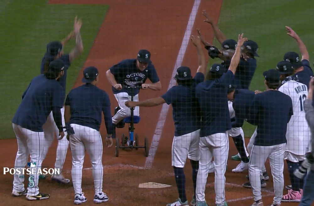 Trent Thornton on his scooter approaching home plate as a crowd of his teammates cheer him on 