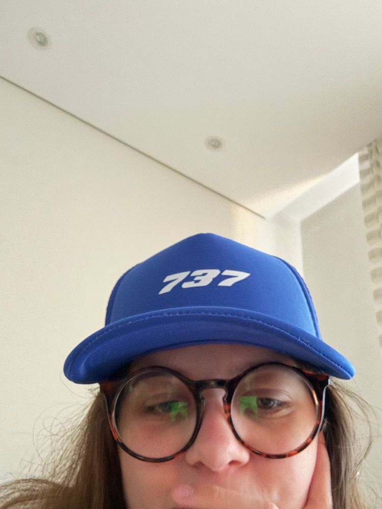 mulher usando óculos redondos e um boné azul escrito 737 em branco