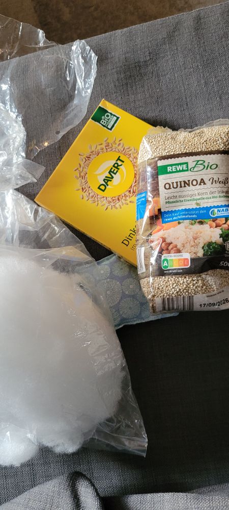 Zwischendrin: ein Bild der Füllwatte,  Quinoa- und Dinkelpackung auf der Couch liegend. Ein kleines Lavendelkissen ist auch zu sehen.
