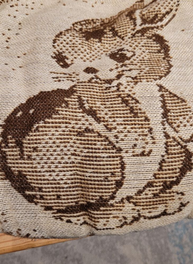 Foto der Vorderseite des Kissens. Esnist fester Stoff in Beige/Braun, virne ist ein Kaninchen in Brauntönen eingewebt.