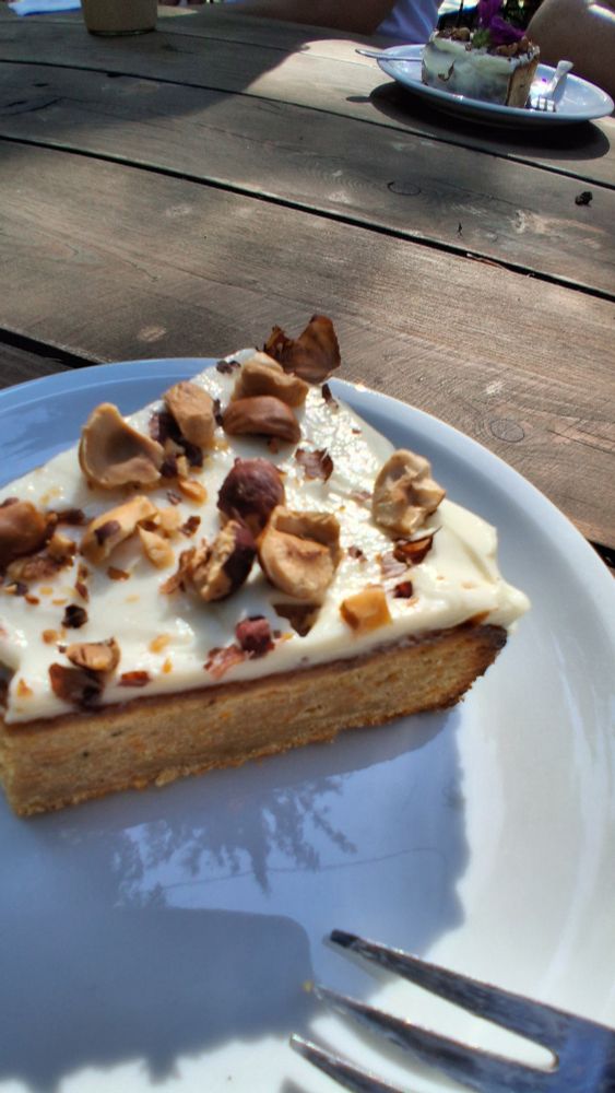 Ein Stück Möhtenkuchen mit Nüssen und weißer Crwme obendrauf auf einem Teller 