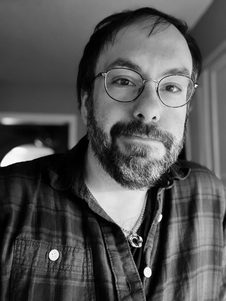 Black and white selfie of me in a button plaid shirt in a dimly light room.