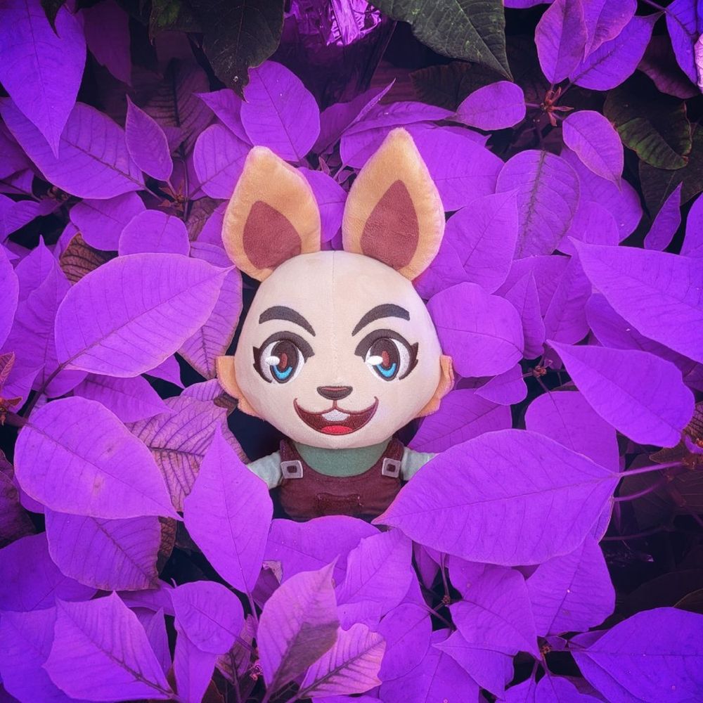 An image of the Gardener Skye plush surrounded by many purple colored leaves.