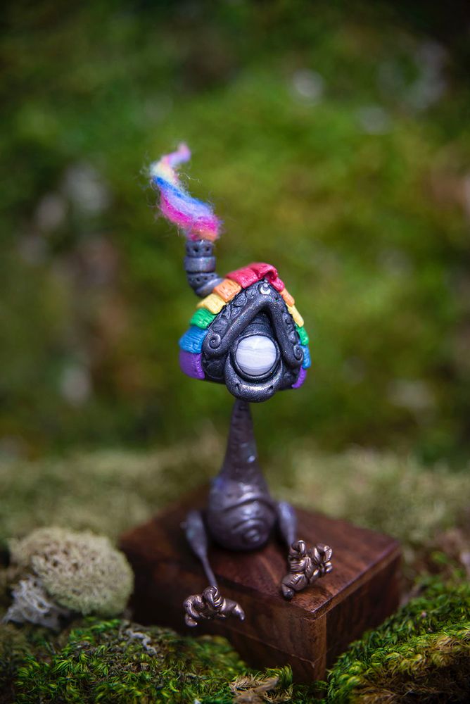 Handmade polymer clay Baba Yaga house figurine sculpted  in Mishes older art style of oversized head with huge, sad eyes, thin neck & limbs, and a plump belly. Sitting under autumn mums. 