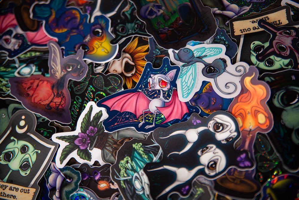 Pile of Mish stickers such as: bat in web, candle, Fresno nightcrawlers, alien, mish on heart, skull flower, angler mermish, sprocket fairy, Wendigo, mandrake, and more!
