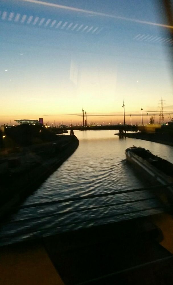 Wind turbines in the port of Antwerp seen through a train window, against the evening sky. Zaha Hadid's Port House is visible on the left.