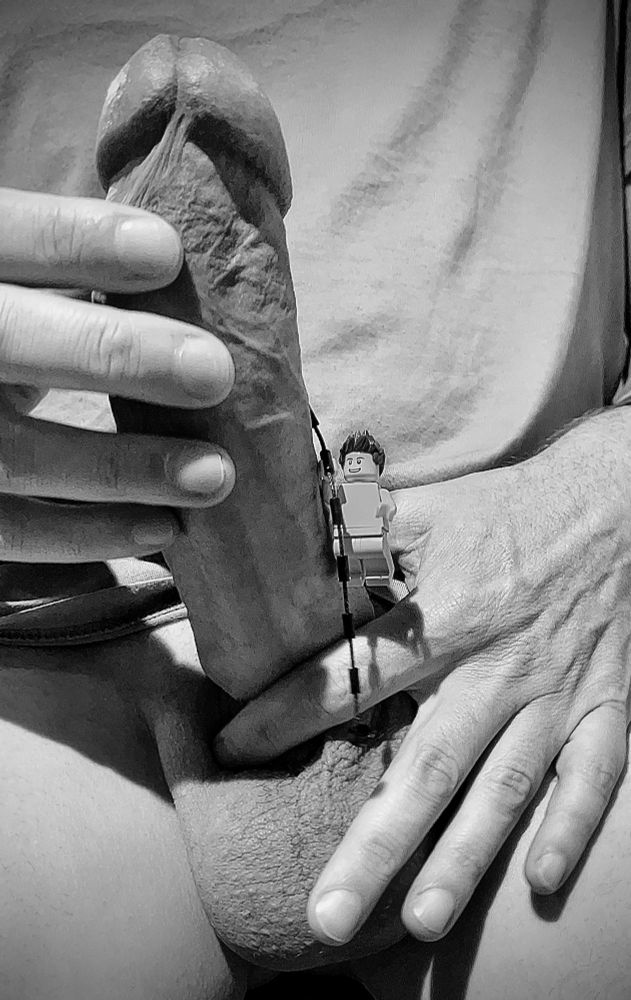 A black and white photo of a naked Lego minifig climbing up my hard cock