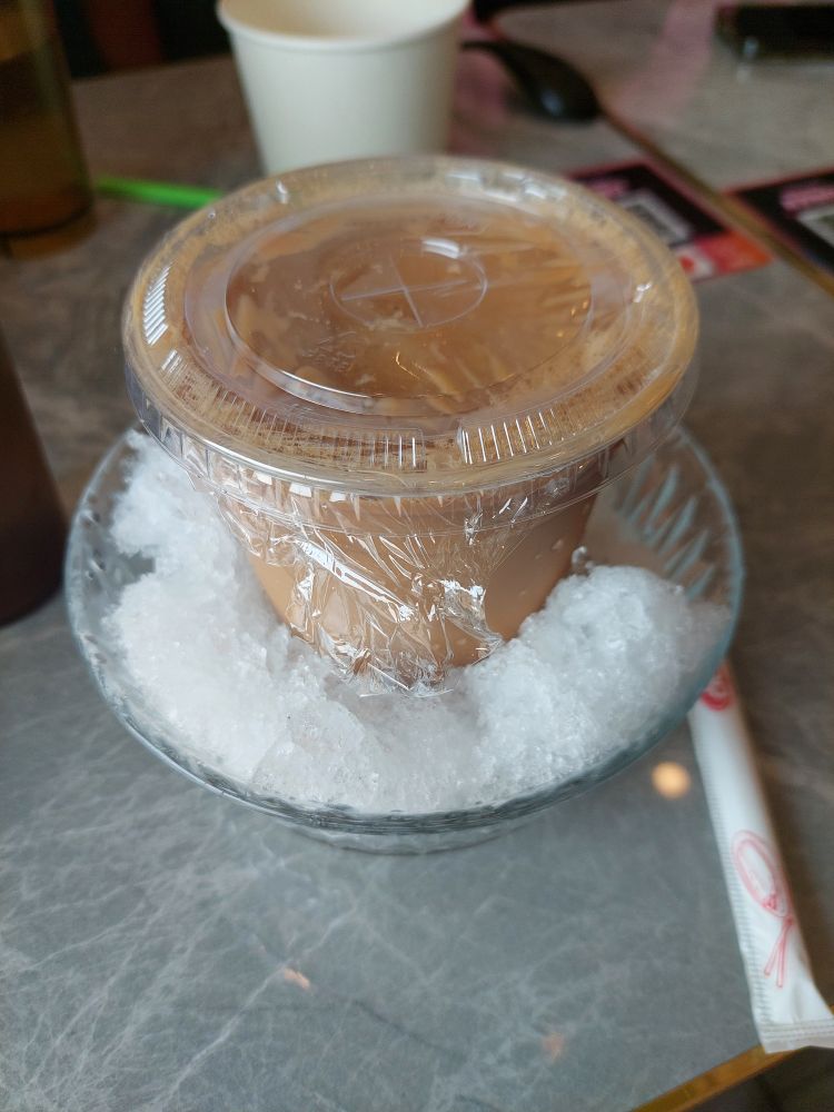 A photo of Iced Hong Kong milk tea in a plastic cup sits in a bowl of shaved ice.