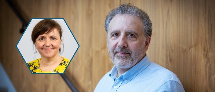A man with short grey hair and a beard stands against a wooden panel background, wearing a light blue shirt. An inset hexagonal frame in the foreground contains a portrait of a woman with short brown hair, wearing a yellow floral blouse and smiling